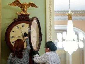 A couple of people stand near a clock Description automatically generated with low confidence