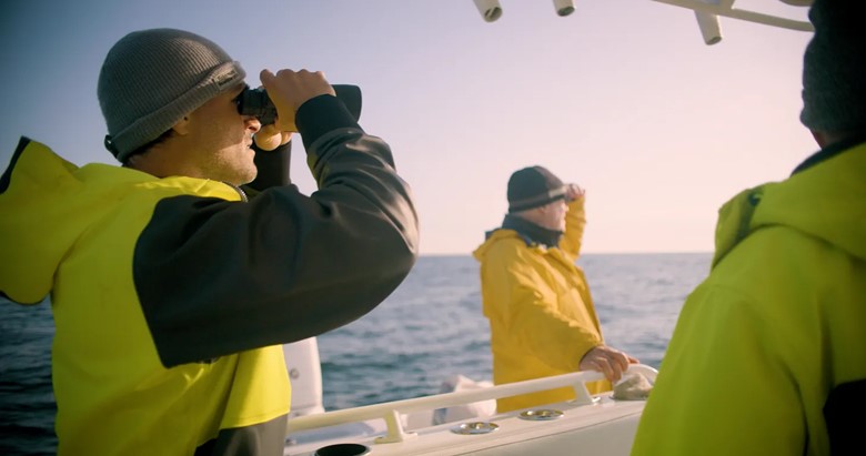 A group of men looking through binoculars on a boat Description automatically generated